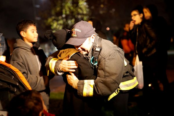A firefighter embraces a child during a vigil for the victims of the fatal warehouse fire.