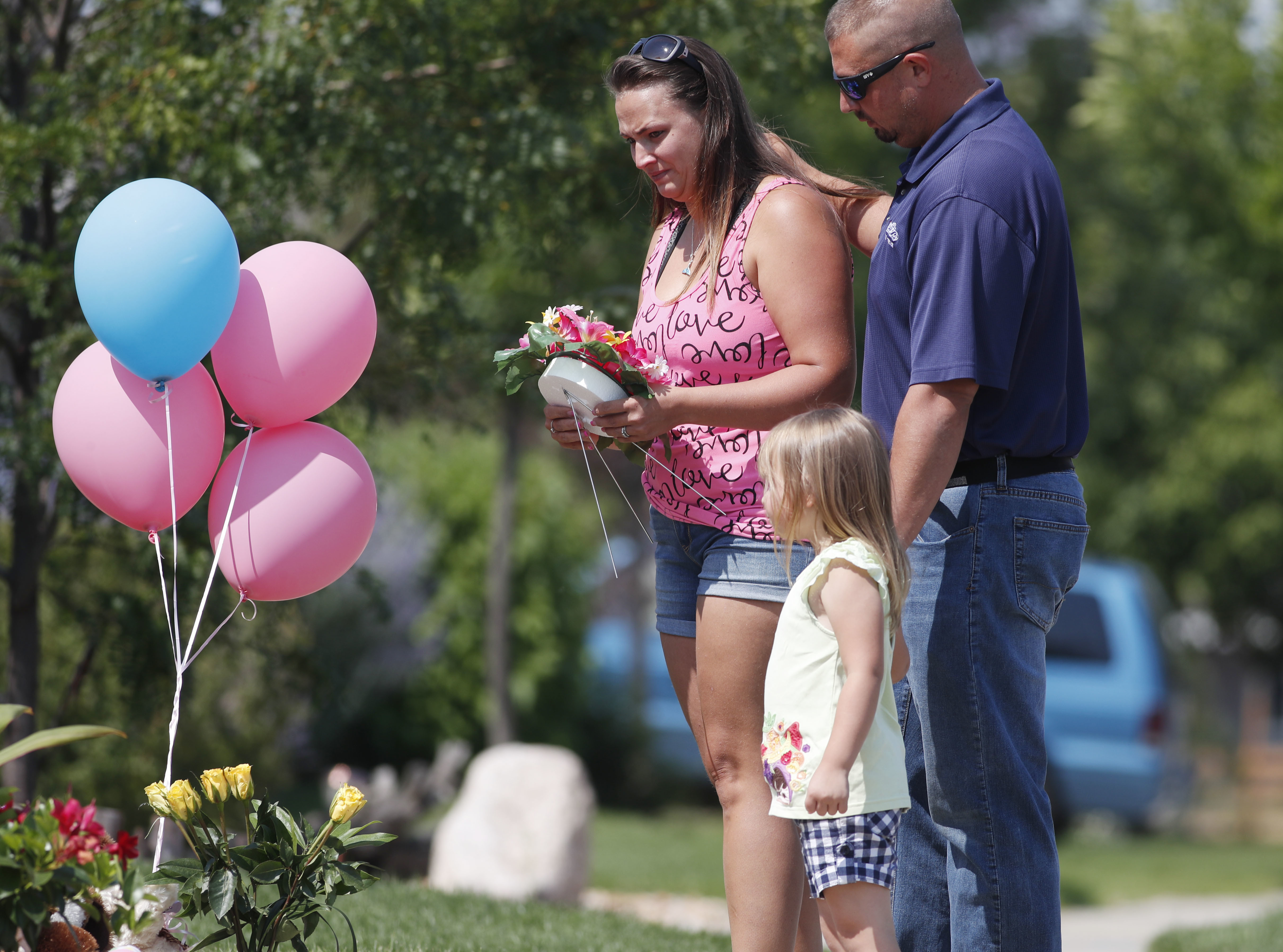 Ashley Bell, left, is consoled by her husband, Steven, and 4-year-old daughter Liberty as the woman places a tribute outside the home where a pregnant woman and her two daughters lived in Frederick, Colorado on Aug. 16, 2018. (AP Photo/David Zalubowski)