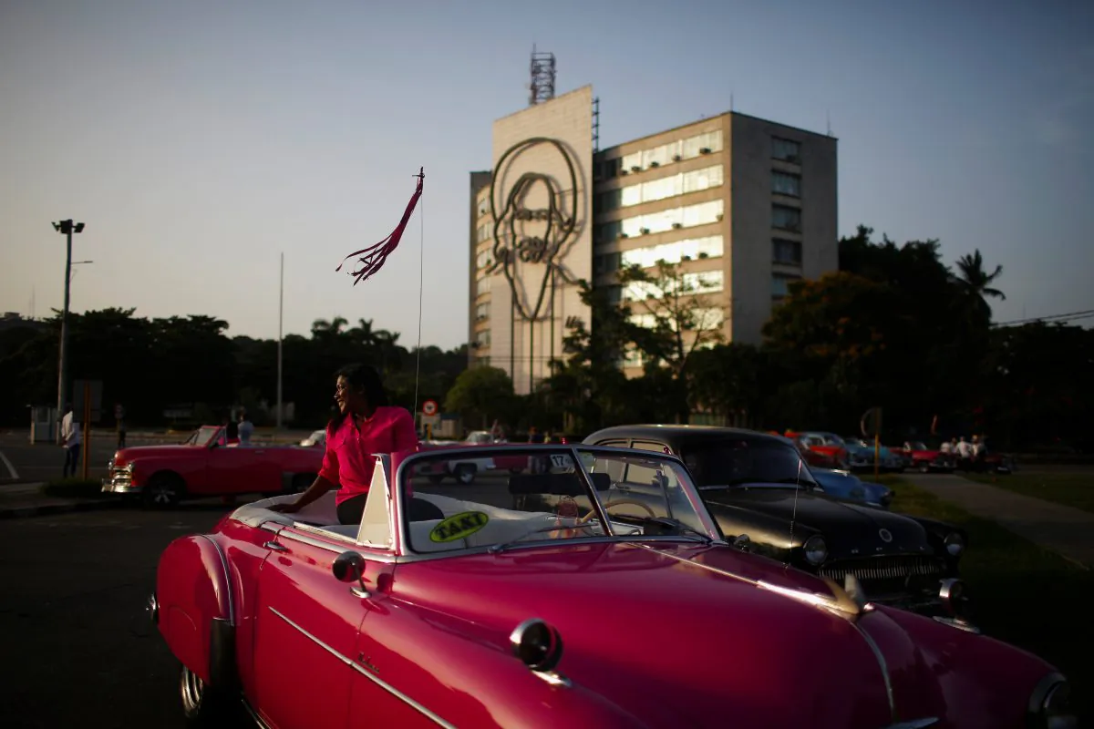 A tourist has a picture taken by a taxi driver in a vintage car at Plaza de la Revolucion in Havana, Cuba August 10, 2018. Picture taken August 10, 2018. REUTERS/Tomas Bravo