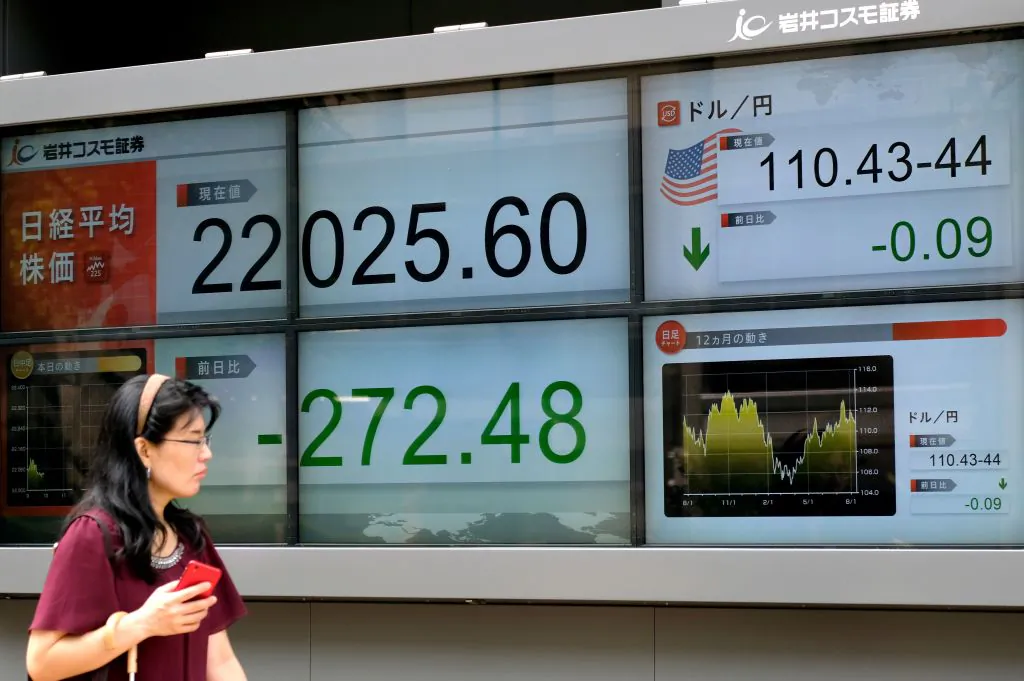 A pedestrian walks past an electronic board showing the share prices of the Tokyo Stock Exchange (L) and the foreign exchange rate between the yen and the US dollar (R) in Tokyo on Aug. 13, 2018. (Kazuhiro Nogi/AFP/Getty Images)