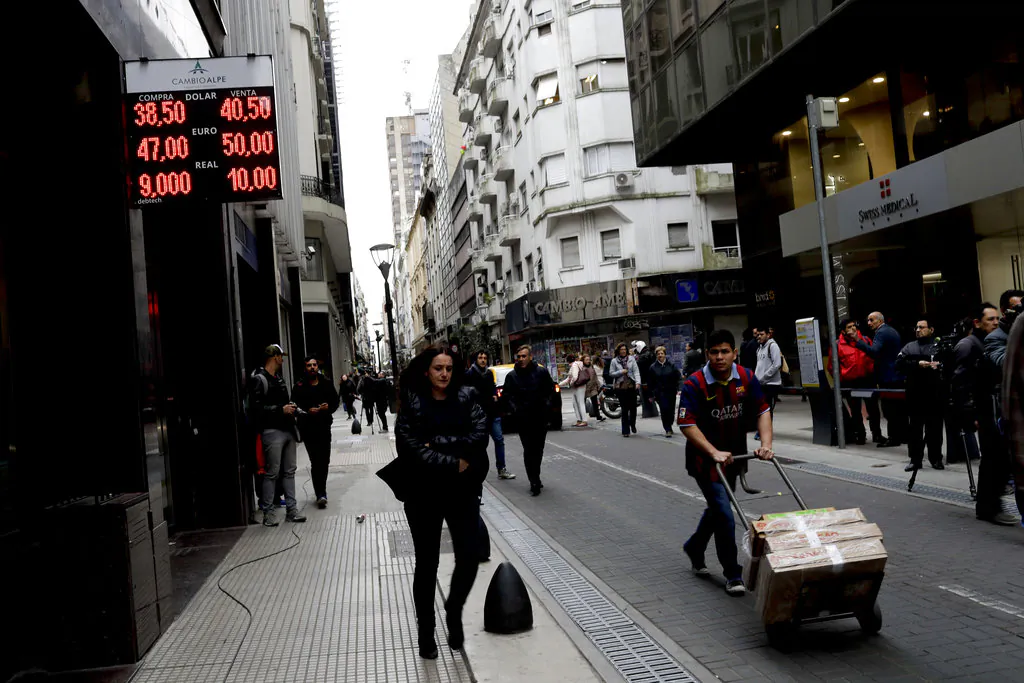People walk past an exchange house in Buenos Aires, Argentina Thursday, Aug. 30, 2018. Argentina's Central Bank increased its benchmark interest rate to 60 percent Thursday as the peso hit a new all-time low. The sharp devaluation of its currency has led prompted Argentina to seek a financing deal with the International Monetary Fund. But the peso keeps tumbling and it has hit markets and investor confidence in Latin America's No. 3 economy.(AP Photo/Natacha Pisarenko)