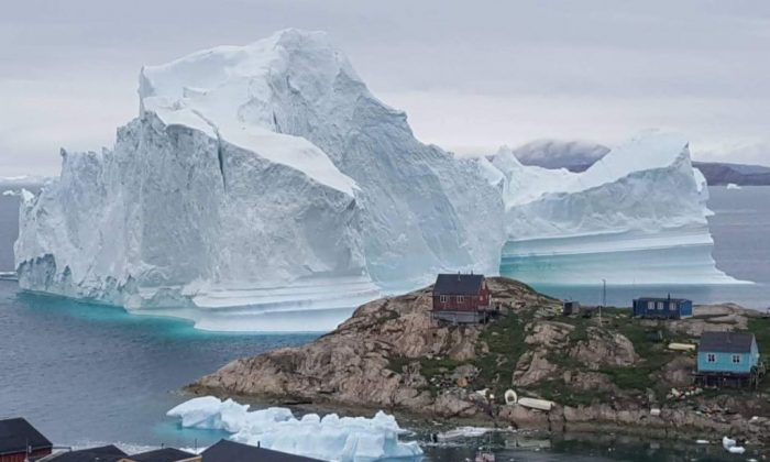 An iceberg behind houses and buildings outside the village of Innarsuit, an island settlement in the Avannaata municipality in northwestern Greenland. (Magnus Kristensen/AFP/Getty Images)