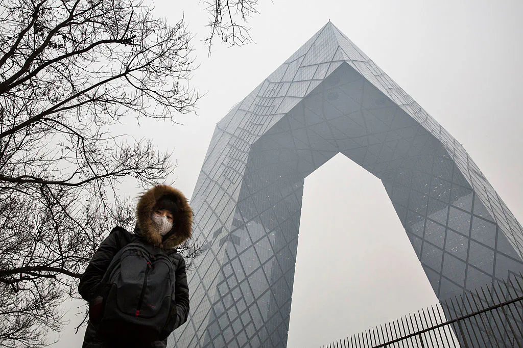 A Chinese woman wears a mask to protect against pollution as she passes the CCTV building in Beijing on Dec. 8, 2015. (Kevin Frayer/Getty Images)