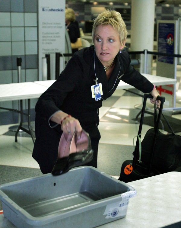 A flight attendant drops her shoes into a plastic tray as she prepares to pass through a security
