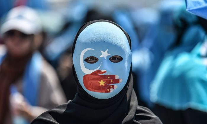 A demonstrator wearing a mask painted with the colours of the flag of East Turkestan and a hand bearing the colours of the Chinese flag attends a protest of supporters of the mostly Muslim Uighur minority and Turkish nationalists to denounce China's treatment of ethnic Uighur Muslims during a deadly riot in July 2009 in Urumqi, in front of the Chinese consulate in Istanbul on July 5, 2018.         (Ozan Kose/AFP/Getty Images)