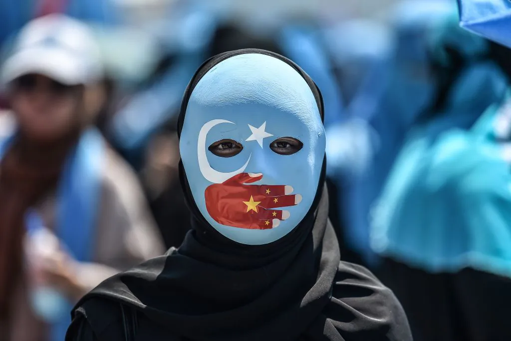 A demonstrator wearing a mask painted with the colours of the flag of East Turkestan and a hand bearing the colours of the Chinese flag attends a protest of supporters of the mostly Muslim Uighur minority and Turkish nationalists to denounce China's treatment of ethnic Uighur Muslims during a deadly riot in July 2009 in Urumqi, in front of the Chinese consulate in Istanbul on July 5, 2018.         (Ozan Kose/AFP/Getty Images)