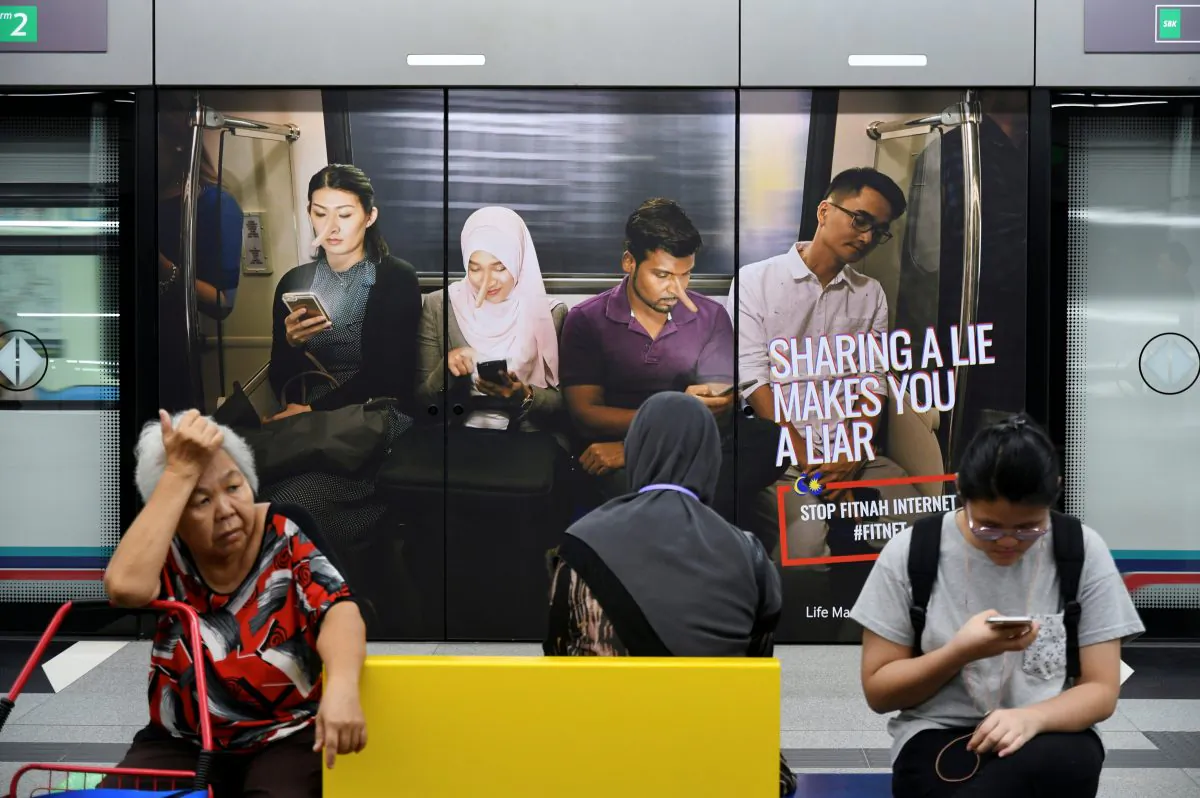 Commuters sit in front of an advertisement discouraging the dissemination of fake news, at a train station in Kuala Lumpur, Malaysia, on March 28, 2018. (Stringer/Reuters)