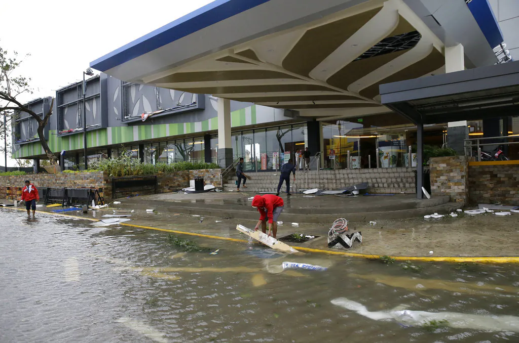 Workers clean up debris outside a mall that got partially damaged by strong winds from Typhoon Mangkhut as it barreled across Tuguegarao city in Cagayan province, northeastern Philippines on, Sept. 15, 2018. (AP Photo/Aaron Favila)