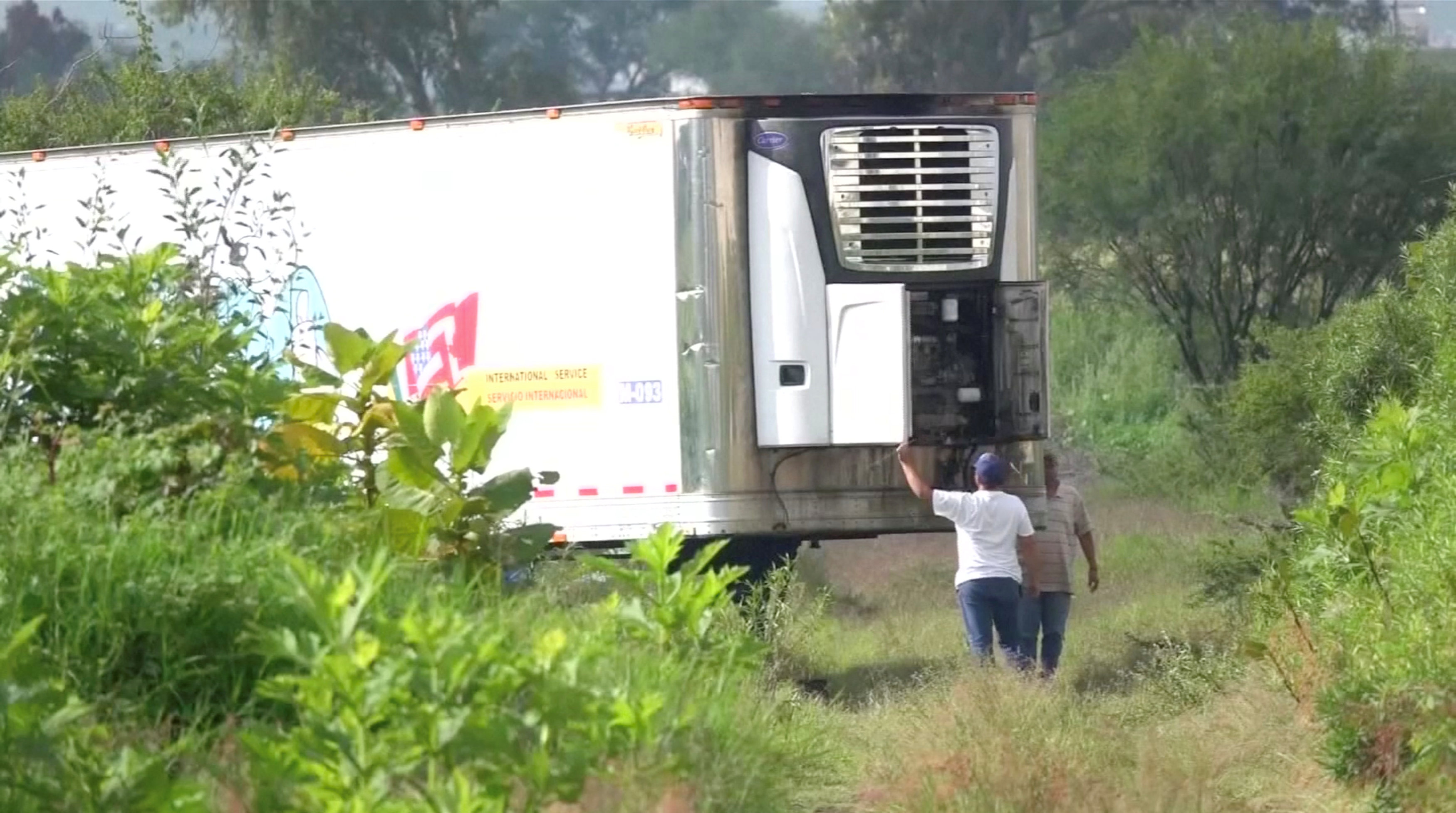 Men stand by an abandoned trailer full of bodies