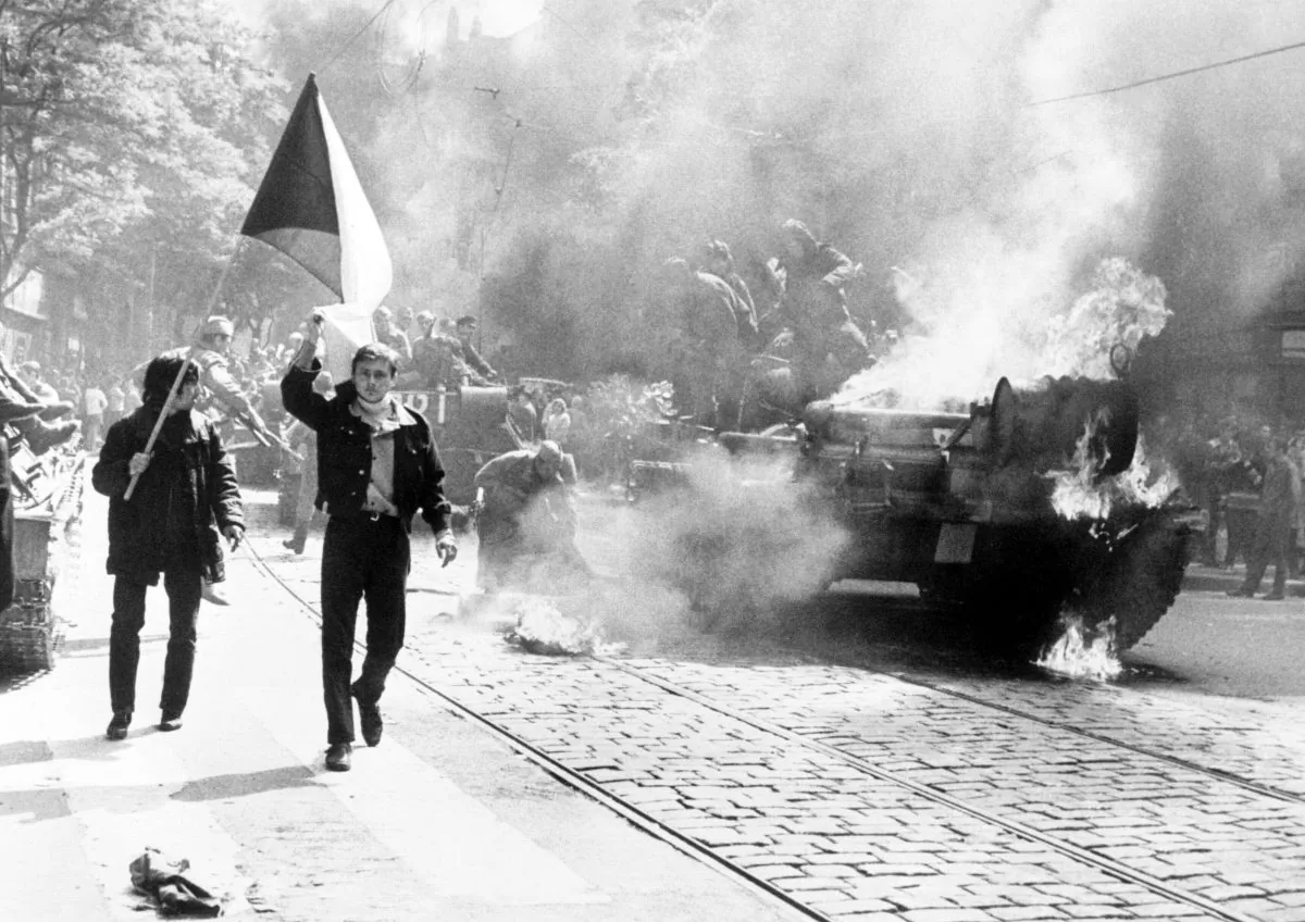 Czechoslovakians carry their national flag past a burning tank in Prague during the Soviet-led invasion of Czechoslovakia in August 1968. (Central Intelligence Agency/Public Domain)