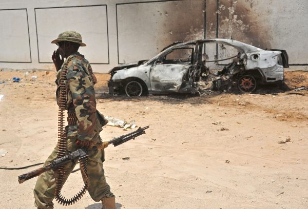A Somali soldier patrols next to the burnt-out wreckage of a car