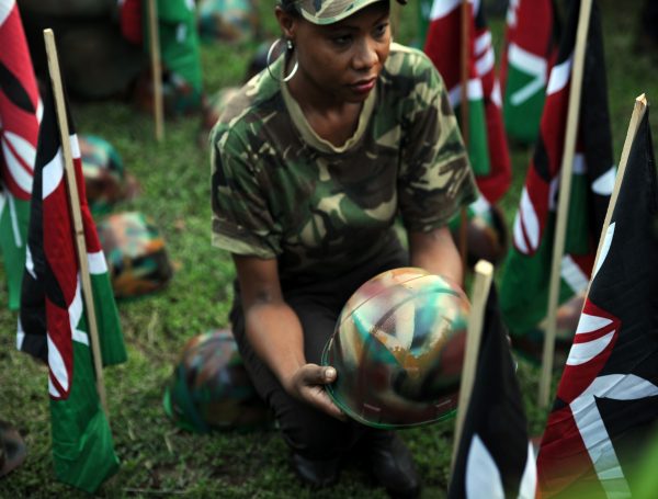 A woman holds a symbolic helmet among Kenyan flags at a vigil .