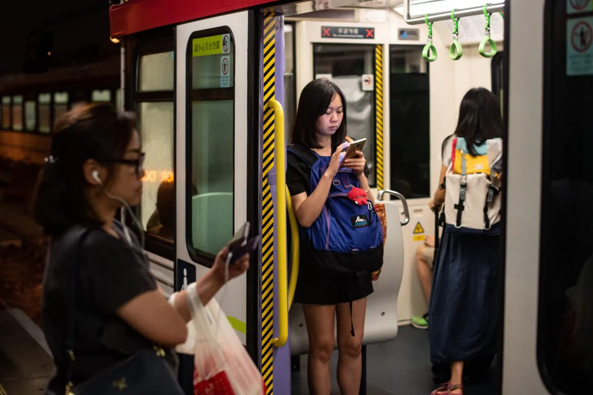 A woman looks at her mobile phone in the MTR's Light Rail as another woman waits at the platform in Tuen Mun district in Hong Kong on August 20, 2018. (PHILIP FONG/AFP/Getty Images)