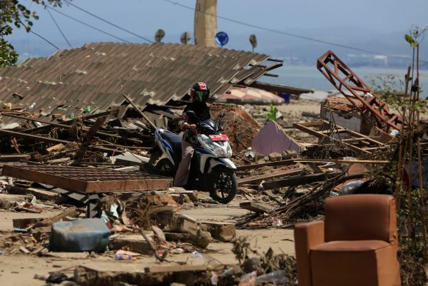 A resident rides a motorcycle amidst debris