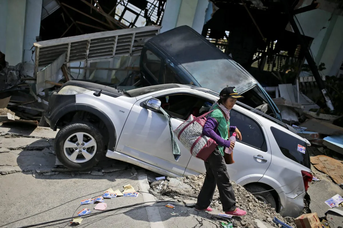 A woman walks past the wreckage of cars which was flattened by Friday's earthquake in Balaroa neighborhood in Palu, Central Sulawesi, Indonesia Indonesia, on Oct. 2, 2018. (Dita Alangkara/AP)