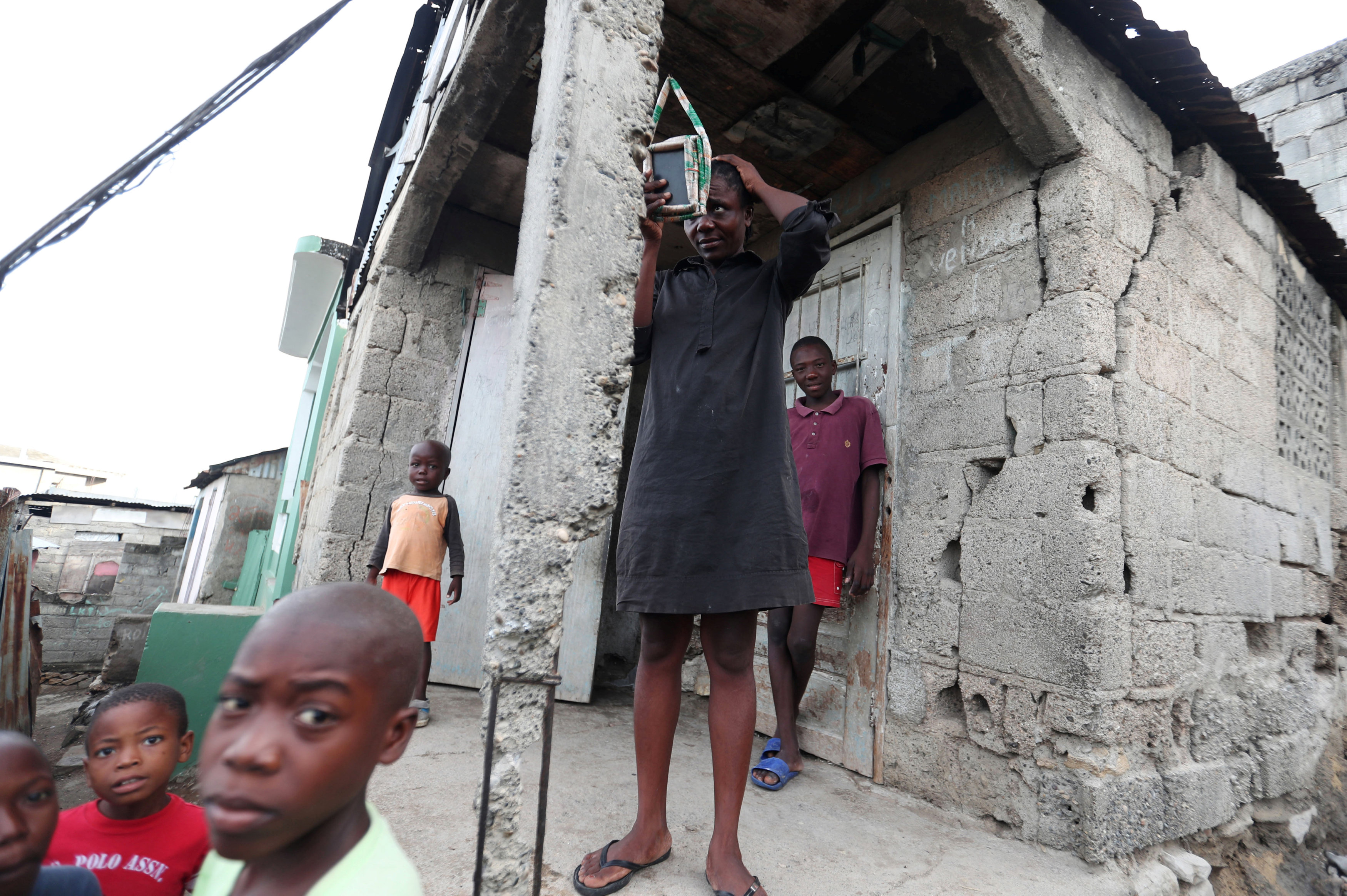 A woman looks at herself in a mirror while standing outside her house after it was damaged in an earthquake, that hit northern Haiti late on Saturday, in Port-de-Paix
