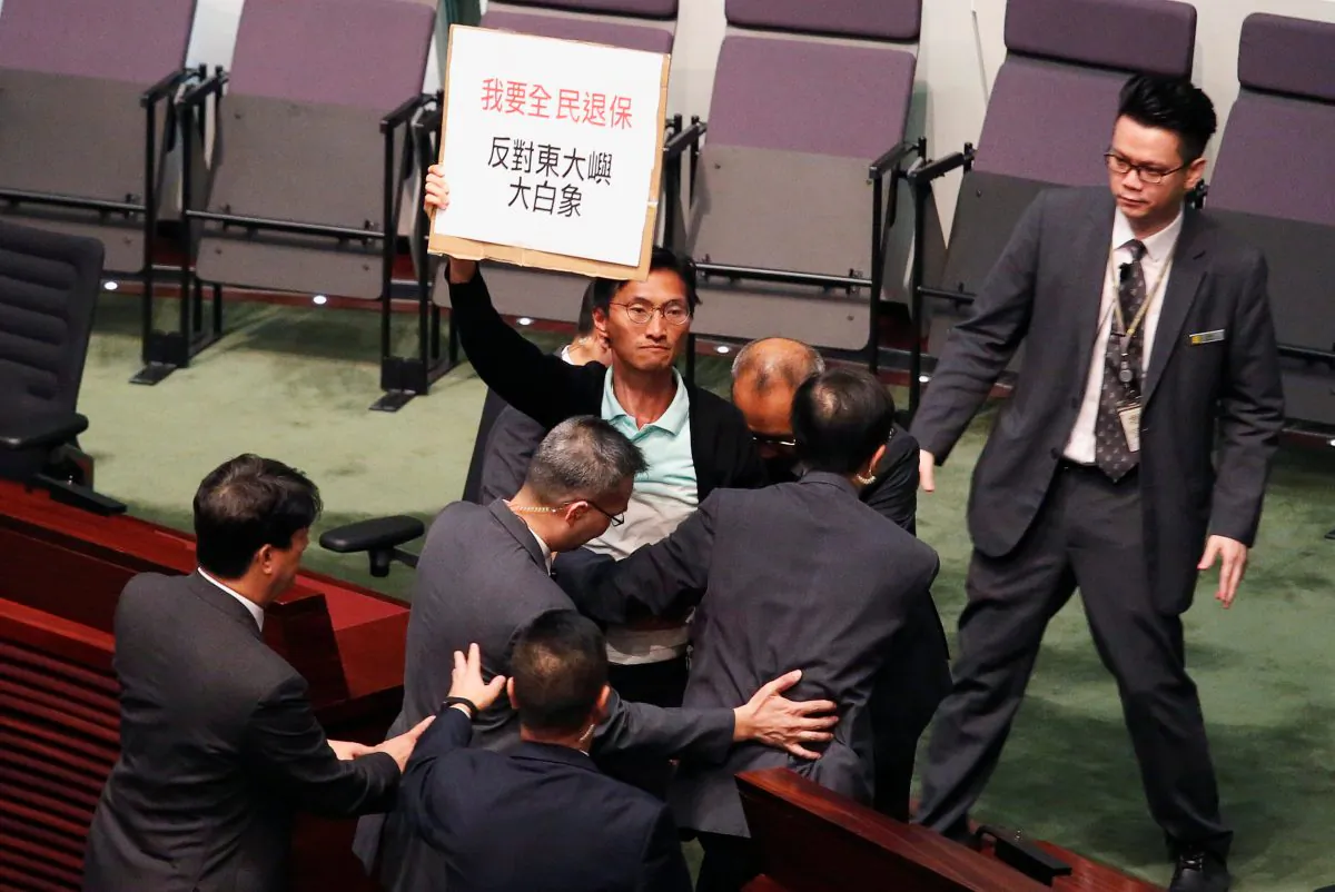 Pro-democracy lawmaker Eddie Chu holding a placard against an East Lantau Metropolis project, is surrounded by security guards at the Legislative Council in Hong Kong, China on Oct. 10, 2018. (Bobby Yip/Reuters)