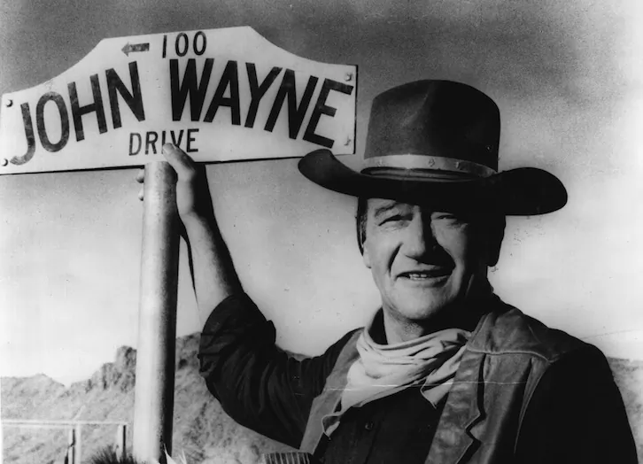 American actor John Wayne stands by the street sign honoring his name in Prescott, Arizona. (Fox Photos/Getty Images)