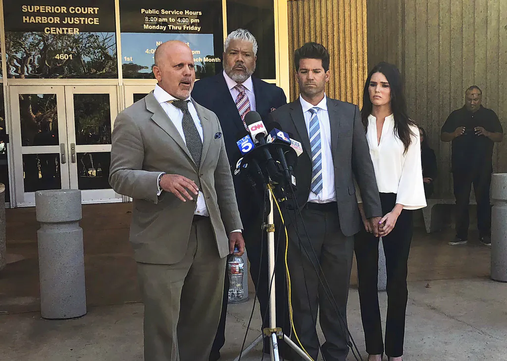 Reality show doctor Grant Robicheaux, second from right, and his girlfriend Cerissa Riley, right, listen as Robicheaux's attorney Philip Cohen, left, speaks outside court in Newport Beach, Calif., following their hearing on new criminal charges involving five additional victims on Oct. 17, 2018. (Amy Taxin/The Associated Press)
