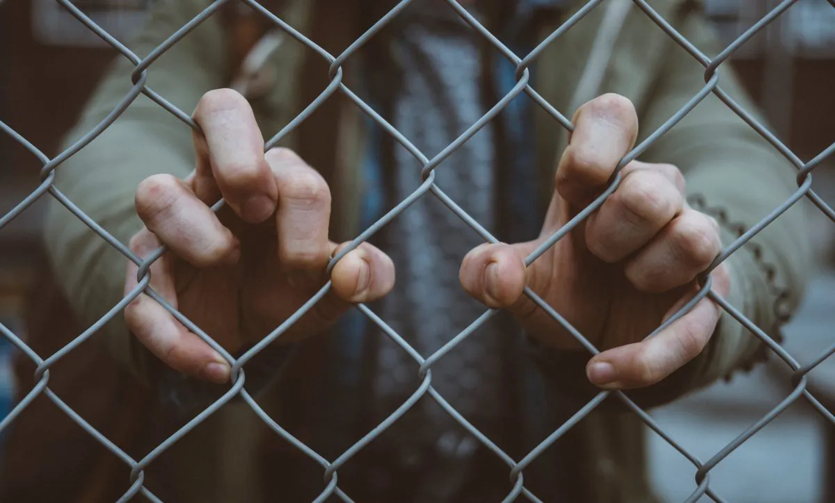 A boy holds onto a chain link fence. (Mitch Lensink/Unsplash)