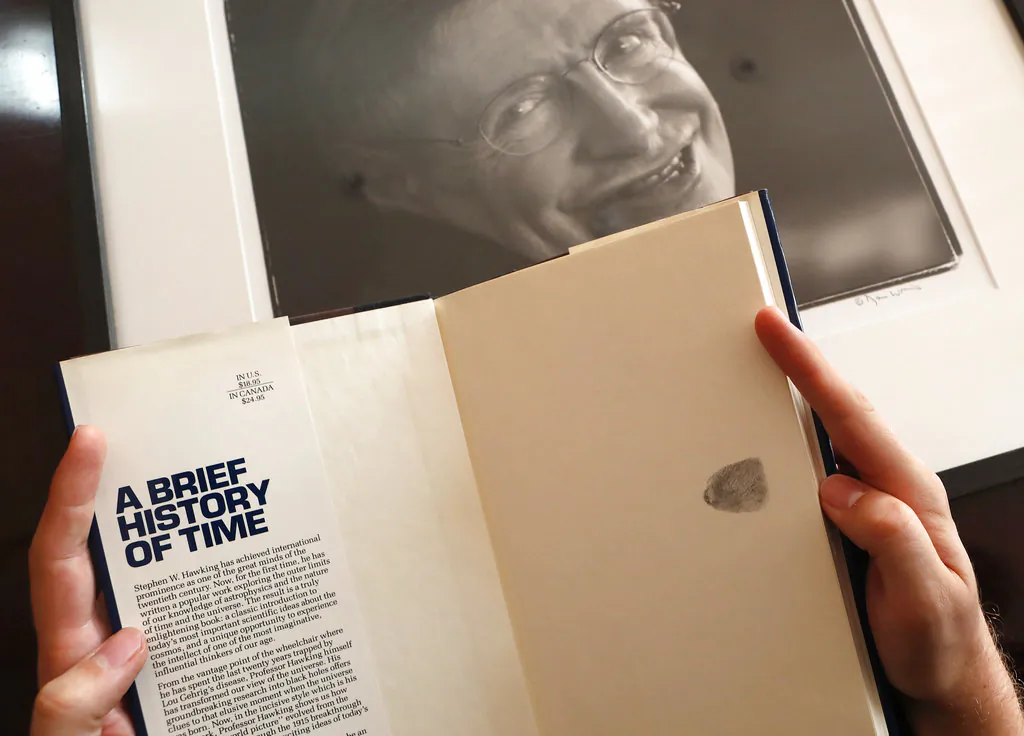 A Book, signed with a thumb print by Stephen Hawking is one of the personal and academic possessions of Stephen Hawking, photo behind, at the auction house Christies in London on Oct. 19, 2018. (AP Photo/Frank Augstein)