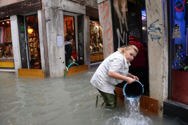 A woman removes water from a shop in a flooded street of Venice