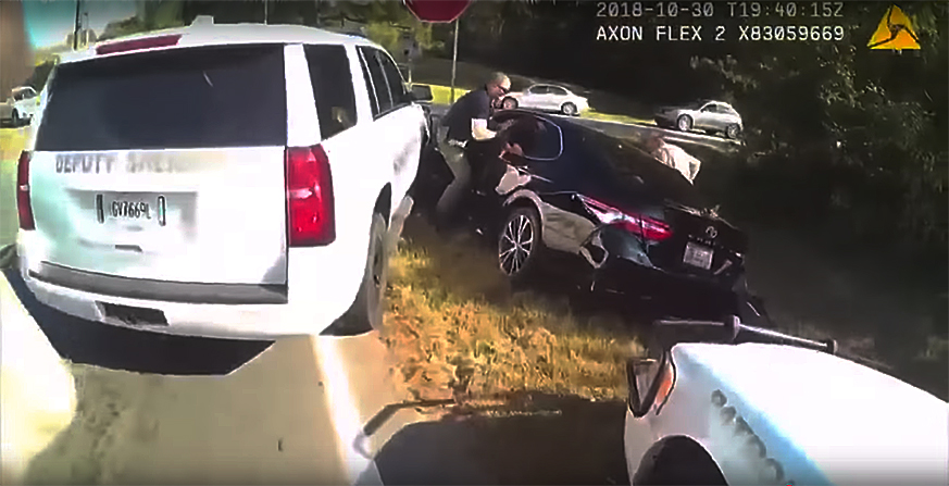 An officer grabs Becker through the car window