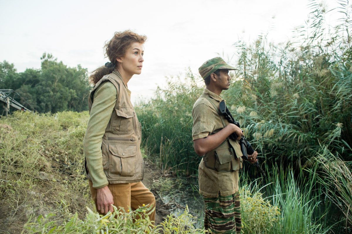 Rosamund Pike standing in war-torn countryside