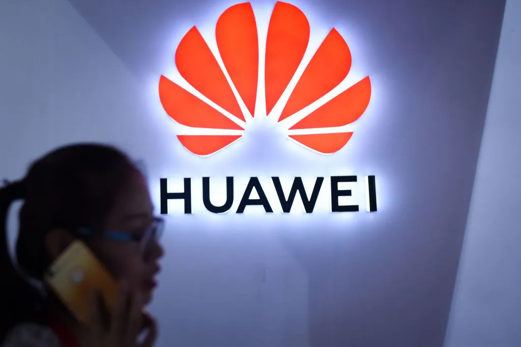 A woman uses her mobile phone in front of a LED display board of Huawei at Beijing International Consumer Electronics Expo in Beijing on July 9, 2018. (Wang Zhao/AFP/Getty Images)