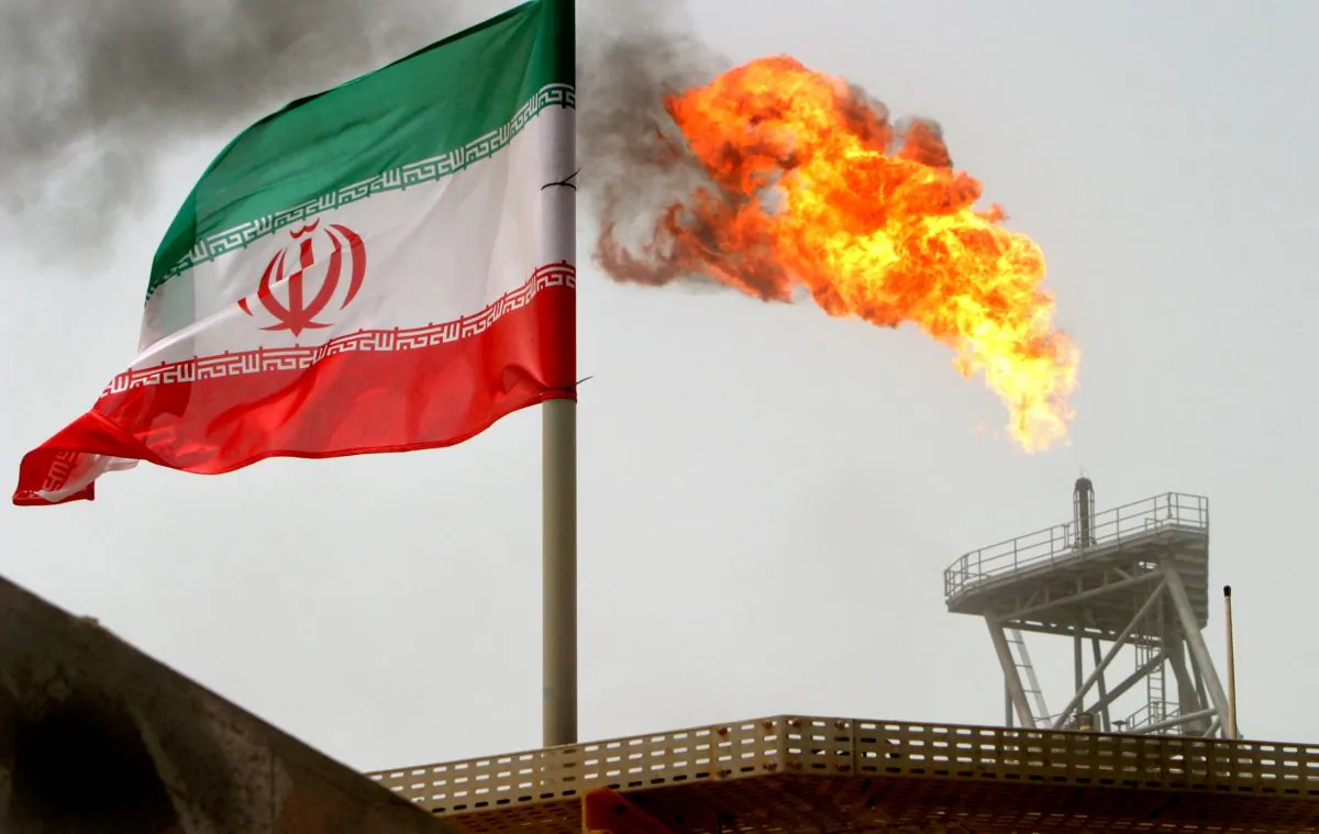 A gas flare on an oil production platform in the Soroush oil fields is seen alongside an Iranian flag in the Persian Gulf, Iran, July 25, 2005. (Raheb Homavandi/File Photo/Reuters)