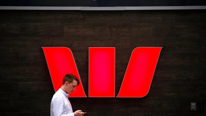 A pedestrian looks at his phone as he walks past a logo for Australia's Westpac Banking Corp located outside a branch in central Sydney, Australia, Nov. 5, 2018. (Reuters/David Gray)