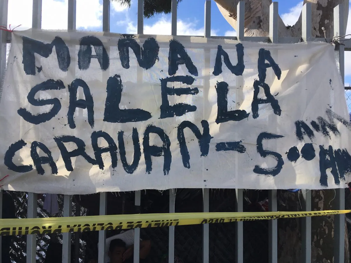 A hand painted sign that says "The caravan leaves at 5 a.m. on Sunday" on the fence around the sports complex where up to 5,000 migrants are camping out in Tijuana Mexico, on Nov. 24, 2018. (Charlotte Cuthbertson/The Epoch Times)