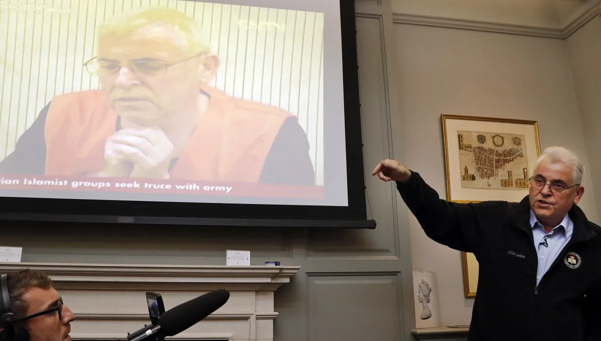British investigator, Peter Humphrey, addresses the media in front of a screen showing him in a Chinese state TV interview, during a press conference in London, on Nov. 23, 2018. (AP Photo/Frank Augstein)