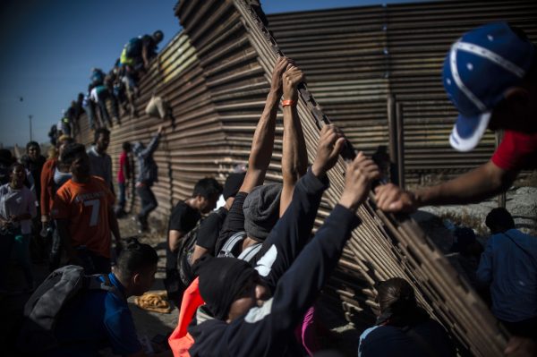 A group of Central American migrants climb the border fence between Mexico and the United States as others try to bring it down, near El Chaparral border crossing, in Tijuana, Baja California State, Mexico