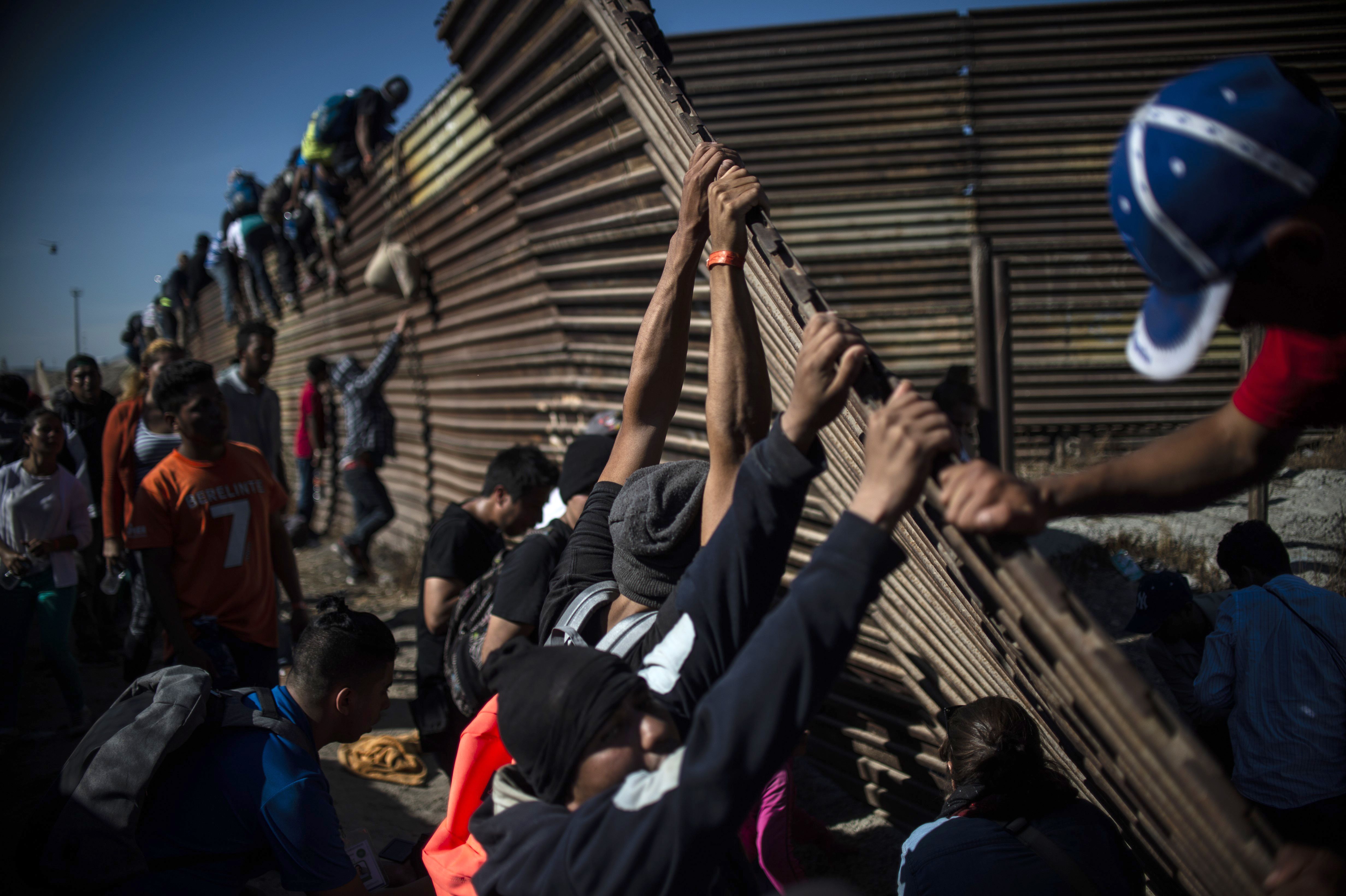 A group of Central American migrants climb the border fence between Mexico and the United States as others try to bring it down, near El Chaparral border crossing, in Tijuana, Baja California State, Mexico