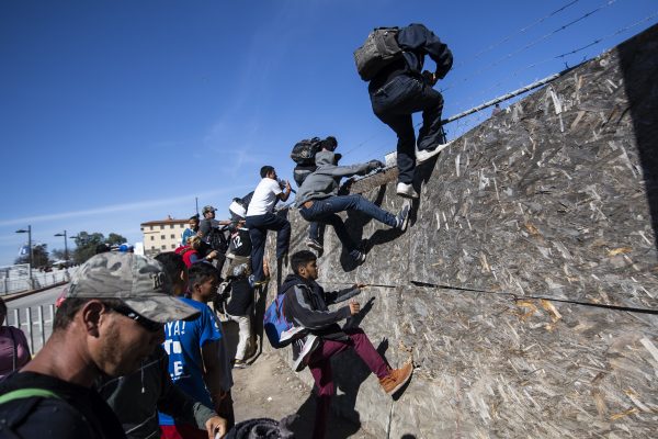 A group of Central American migrants -mostly from Honduras- get over a fence