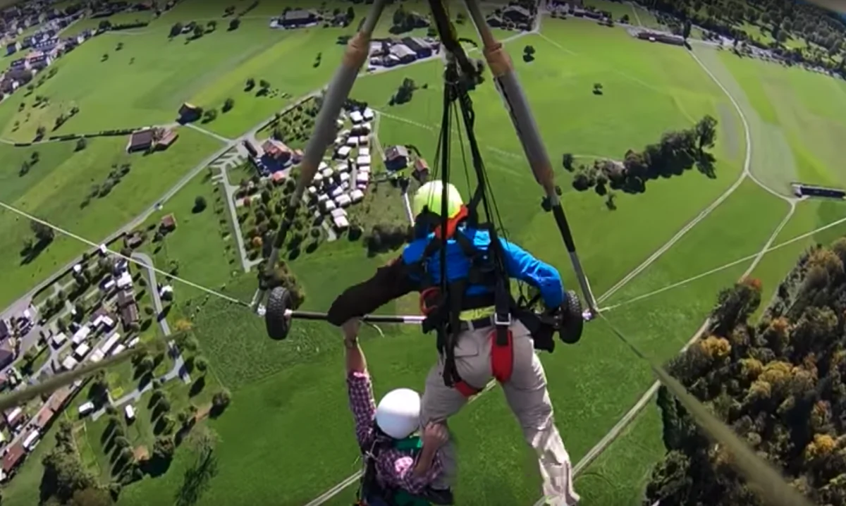 YouTuber Chris Gursky hangs from the bar of the hang-glider and his pilot's leg over the Swiss countryside in Oct. 2018. (Screengrab/YouTube/Chris Gursky)