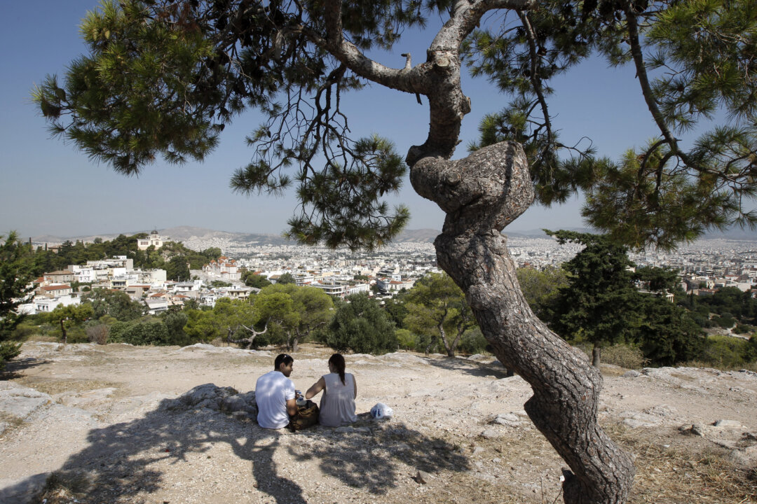Tourists sit under a pine tree on a hill overlooking Athens on July 7, 2011. (Reuters/John Kolesidis)