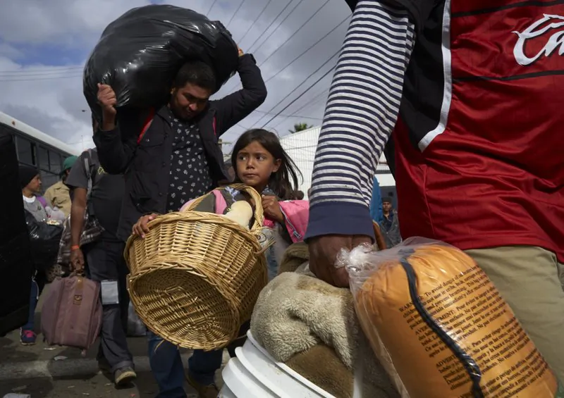 Brittany Rios, of Honduras, center, carries stuffed animals in a wicker basket as her family leaves a shelter for members of the Central American migrant caravan in Tijuana, Mexico, on Nov. 30, 2018. (AP Photo/Gregory Bull)