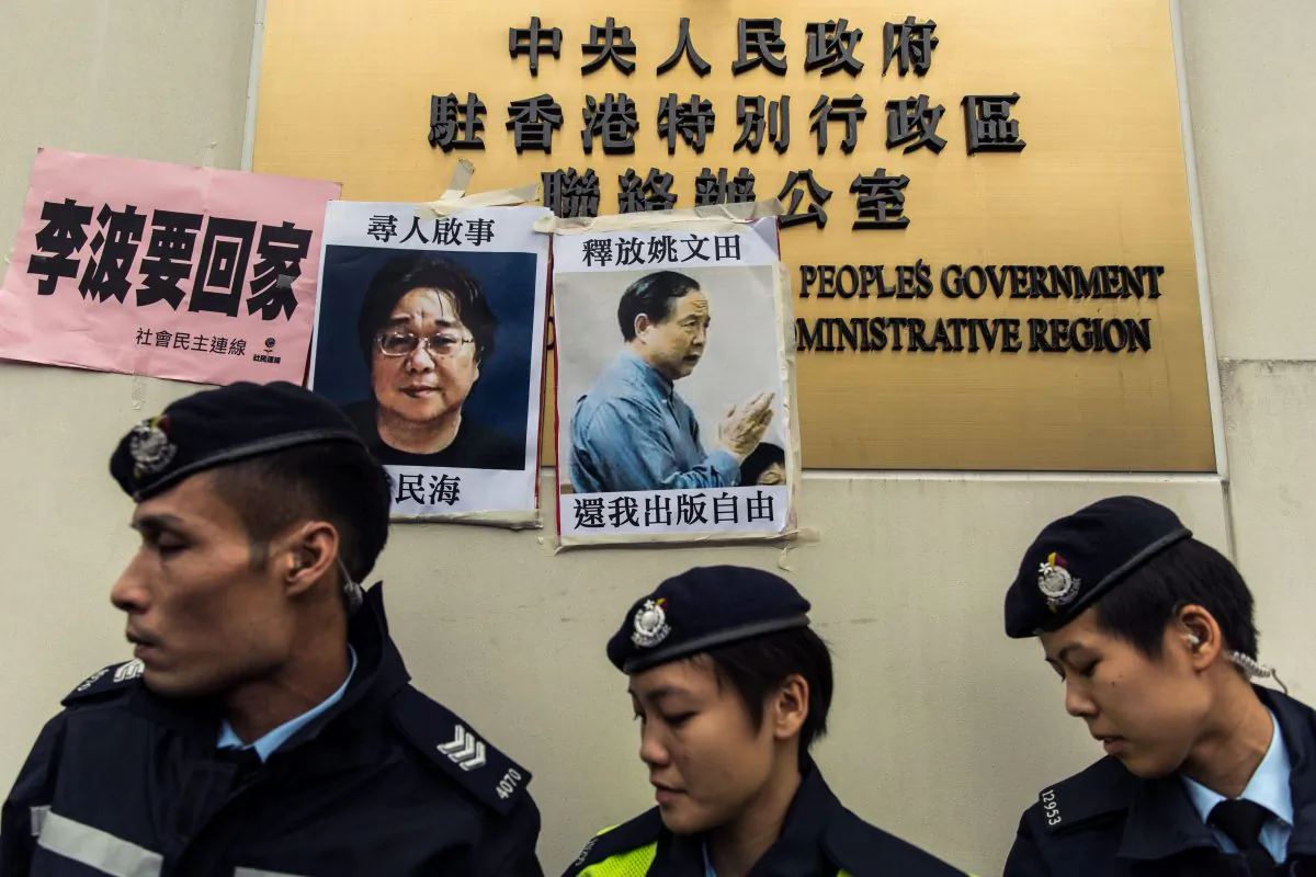 Police walk past missing person notices of Gui Minhai (L), one of five missing booksellers from the Mighty Current publishing house, and Yau Wentian (R), a Hong Kong publisher who was last year jailed for 10 years while preparing to release a book critical of Chinese leadership, posted on top of the sign of China's Liaison Office in Hong Kong on Jan. 3, 2016. (ANTHONY WALLACE/AFP/Getty Images)