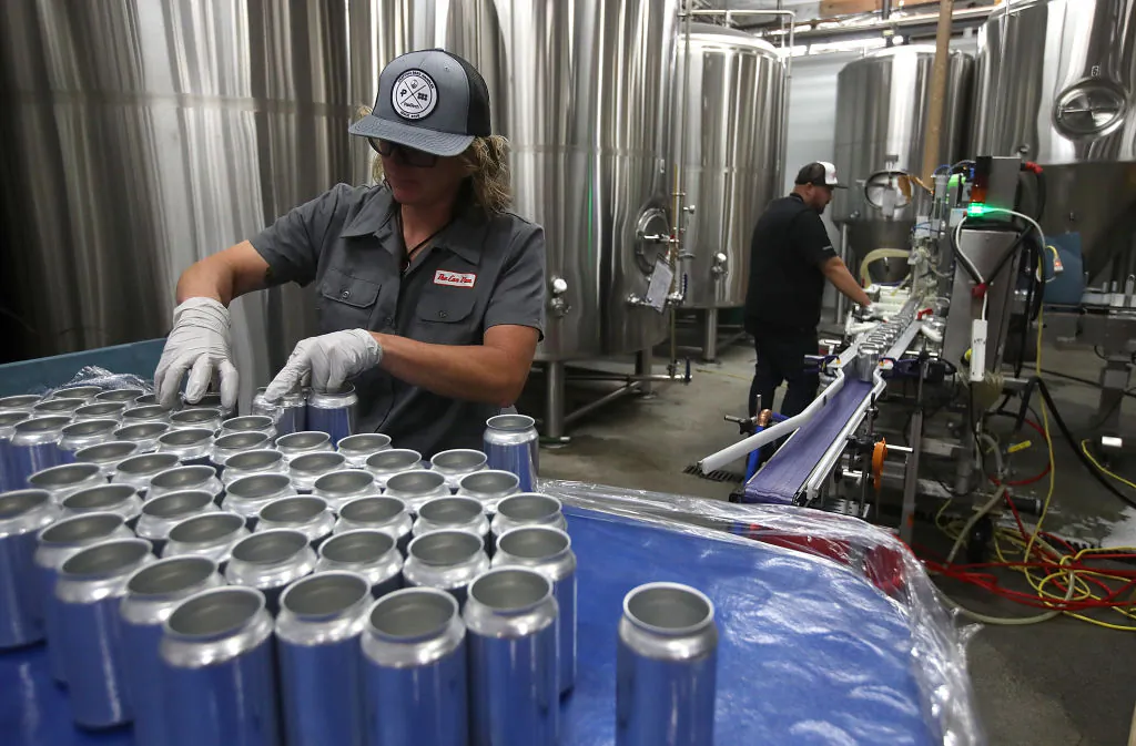 Kathryn Fisher with Can Van, a mobile canning company, places empty aluminum cans on a conveyor belt to be filled with beer at Devil's Canyon Brewery in San Carlos, California, on June 6, 2018. (Justin Sullivan/Getty Images)