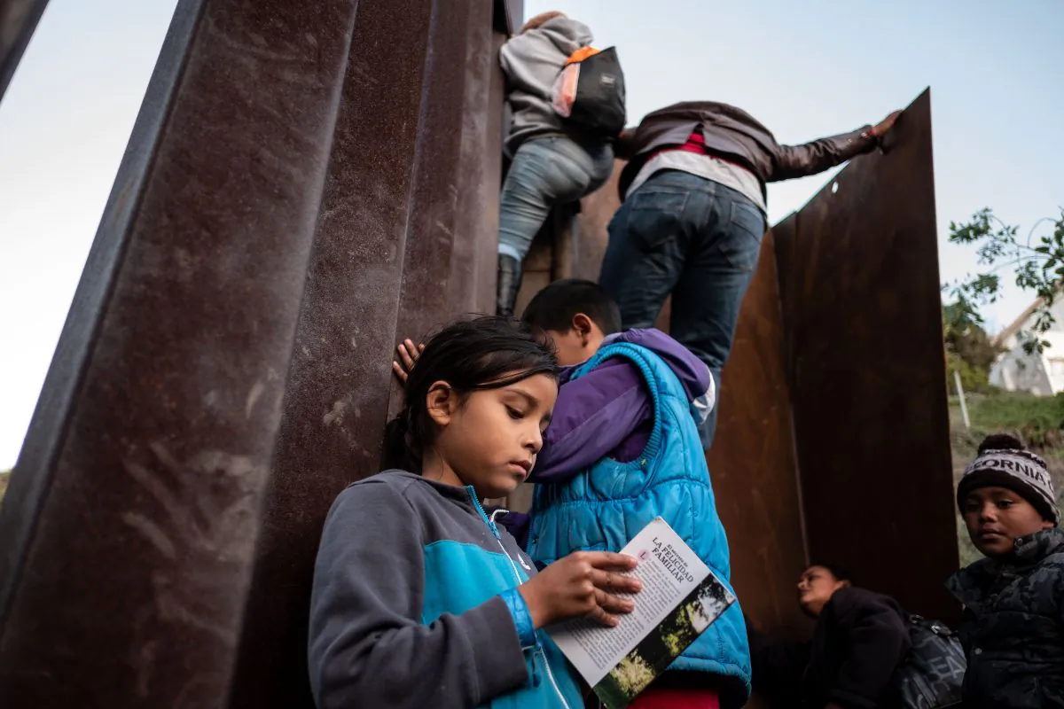 A Central American migrant girl holds a book as other migrants travelling in a caravan, climb the Mexico-US border fence in an attempt to cross to San Diego County, in Playas de Tijuana, Baja California state, Mexico on Dec. 12, 2018. (Guillermo Arias/AFP/Getty Images)