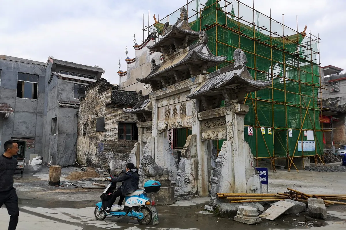 A woman rides a motorcycle past an imperial-style arch and a building under renovation in Rucheng county, Hunan Province, China on Dec. 3, 2018. (Shu Zhang/Reuters)