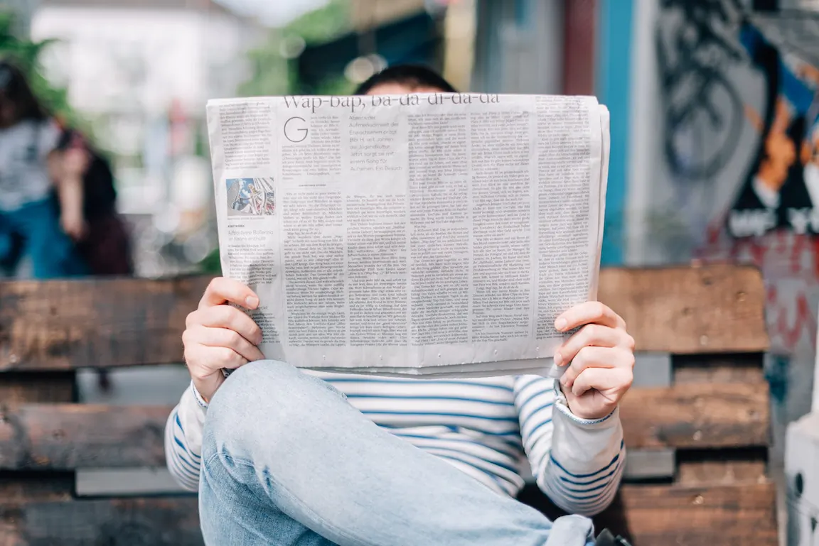 A man reads a newspaper while sitting on a bench. (Roman Kraft/Unsplash)