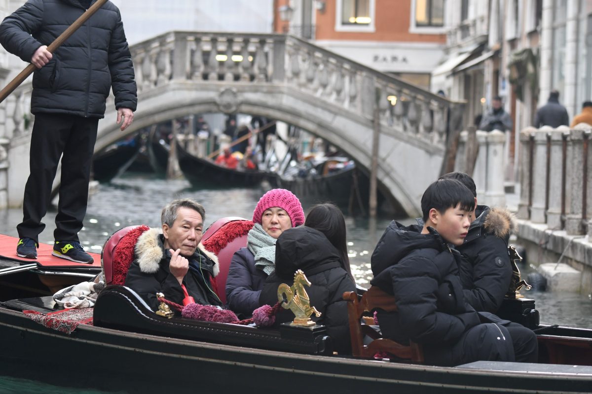 A group of tourists sits on a gondola sailing on a canal of Venice
