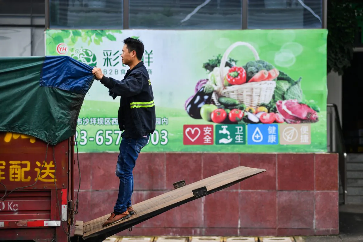 A worker adjusts a cover on the back of a truck outside a warehouse of Yonghui Superstores in Chongqing, China on Oct. 9, 2018. (Reuters)