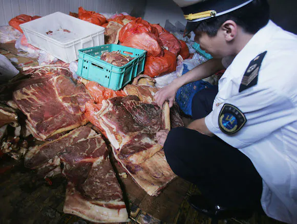 An officer with the Beijing Health Supervision Institute inspects spoiled pork at a freezer of the Huilongguan Chengbei Trade Market on July 28, 2005 in Changping County of Beijing, China. (China Photos/Getty Images)