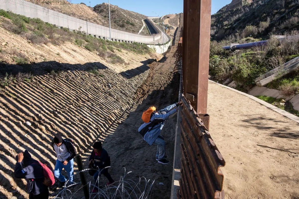 Central American migrants hoping to reach the United States cross the US-Mexico border fence from Tijuana (R), Baja California State, Mexico, to the U.S., on Dec. 30, 2018. (GUILLERMO ARIAS/AFP/Getty Images)