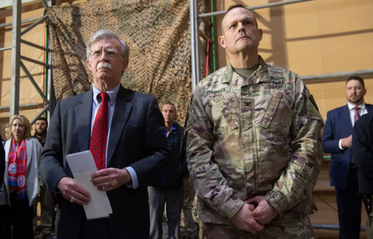 US National Security Adviser John Bolton (L) listens as US President Donald Trump speaks to members of the US military during an unannounced trip to Al Asad Air Base in Iraq on Dec. 26, 2018. (Saul Loeb/AFP/Getty Images)