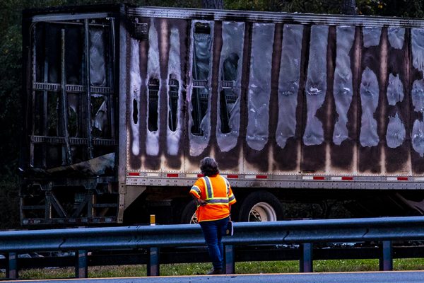 A worker looks at a charred semi-truck after a wreck with multiple fatalities